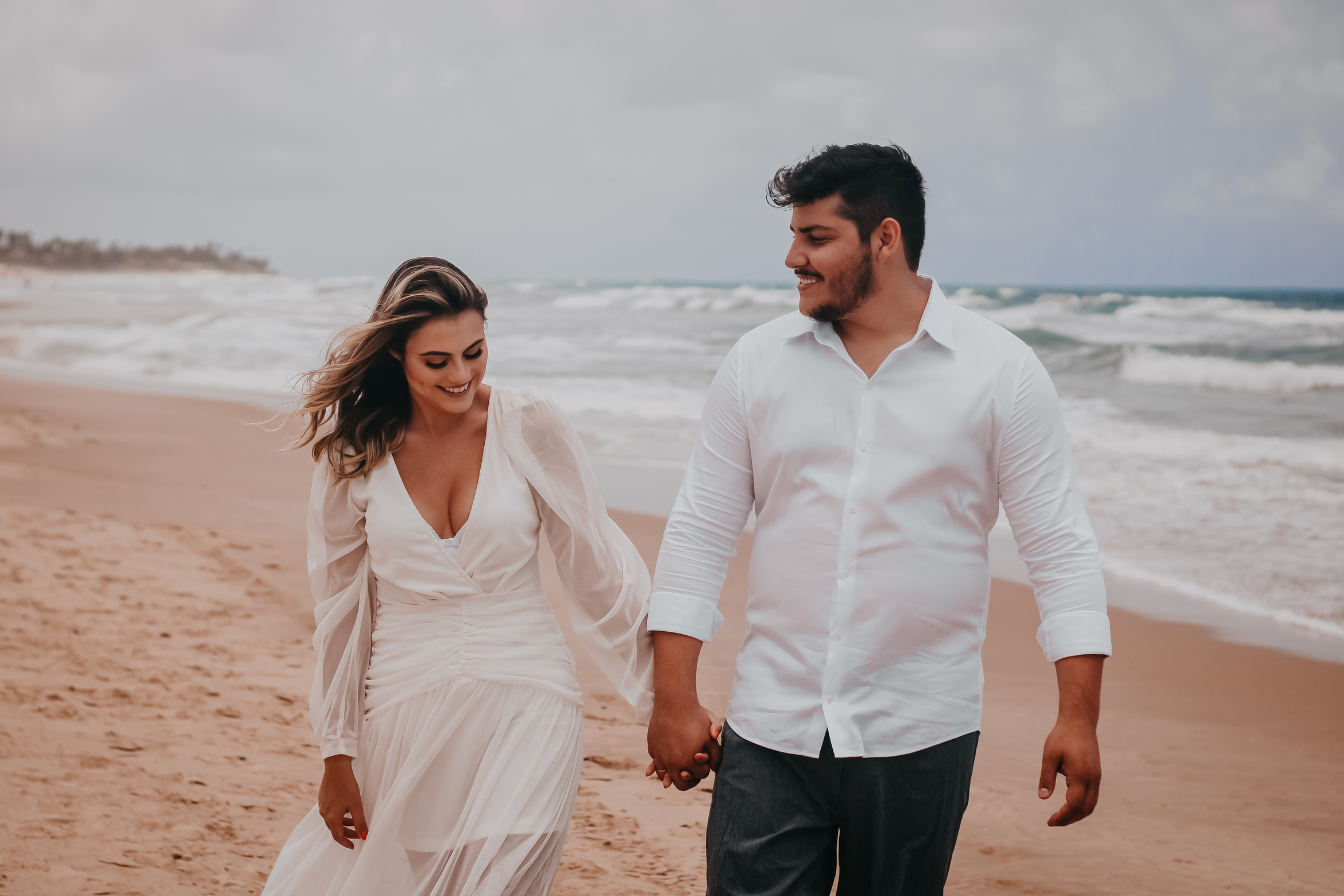 Smiling couple holding hands while walking along seaside